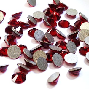 Könnte beinhalten: Eine Streuung von roten Kristall-Straßsteinen mit silbernen Kleberücken. Die Strasssteine sind facettiert und haben eine glänzende Oberfläche.