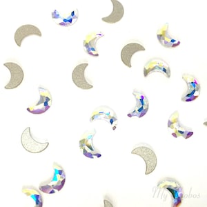 May include: A scattering of iridescent crescent moon shaped rhinestones and silver crescent moon shaped embellishments on a white background.