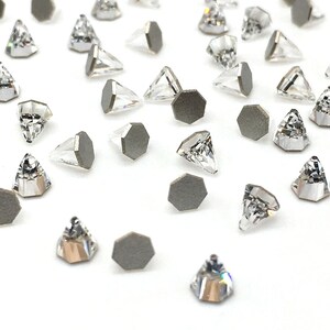 May include: A collection of clear crystal rhinestones with silver settings. The rhinestones are triangular in shape and have a pointed tip. The settings are hexagonal and have a flat back.