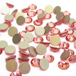 Puede incluir: Una gran cantidad de pequeñas piedras de cristal redondas de color rosa claro con un acabado mate. Las piedras de cristal están esparcidas sobre una superficie blanca.