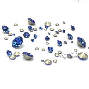 Puede incluir: Surtido de piedras de cristal azules y plateadas de varios tamaños. Las piedras de cristal están esparcidas sobre una superficie blanca.