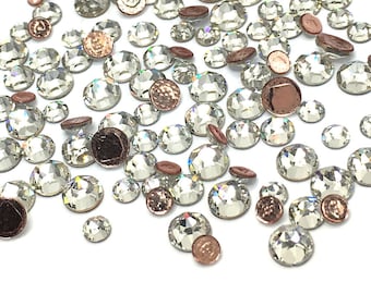 Puede incluir: Una dispersión de piedras de cristal transparentes con un efecto arcoíris iridiscente. Algunas de las piedras tienen un respaldo de cobre.