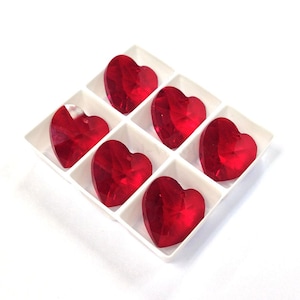 May include: Six red heart-shaped glass crystals in a white plastic tray. The crystals are faceted and have a shiny finish.
