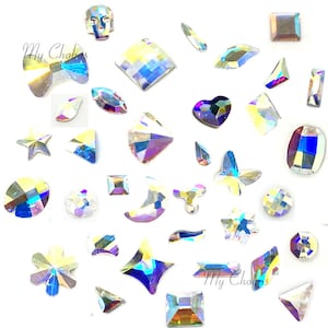 May include: Assortment of iridescent glass rhinestones in various shapes, including stars, hearts, moons, butterflies, and skulls. The rhinestones are scattered on a white background.