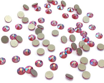 May include: A scattering of small, round, iridescent red rhinestones with silver backs. The rhinestones are scattered on a white background.