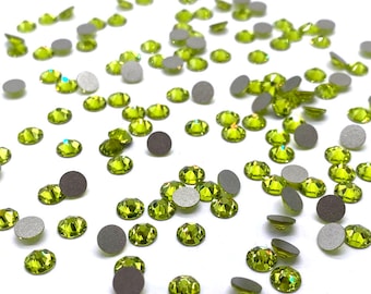 Puede incluir: Una dispersión de piedras de cristal verdes con engastes plateados. Las piedras de cristal están dispersas sobre una superficie blanca.