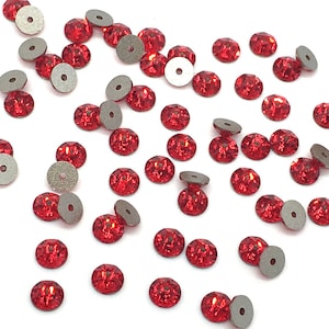 May include: A scattering of red crystal rhinestones with silver settings. The rhinestones are scattered on a white background.