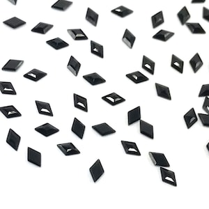 May include: A scattering of black diamond-shaped rhinestones on a white background.