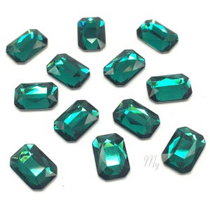 May include: A collection of emerald green rectangular rhinestones. The rhinestones are faceted and have a shiny finish.