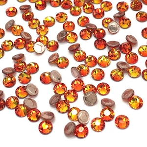 May include: A scattering of orange and yellow crystal rhinestones with a flat, silver backing. The gemstones are round and faceted, reflecting light. Some have a visible silver backing. Ideal for crafting and embellishments.