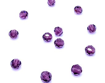 Può includere: Una collezione di undici piccole perline rotonde sfaccettate di un colore viola traslucido intenso. Ogni perlina presenta molteplici superfici piatte che catturano la luce, creando un effetto scintillante sui pezzi sparsi su una superficie piana.