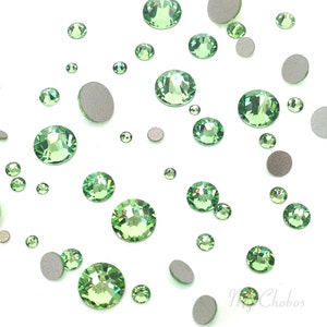 May include: Assortment of green rhinestones of various sizes, scattered on a white background.