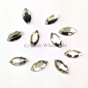 May include: A collection of 10 clear marquise-shaped rhinestones. The rhinestones are scattered on a white surface.