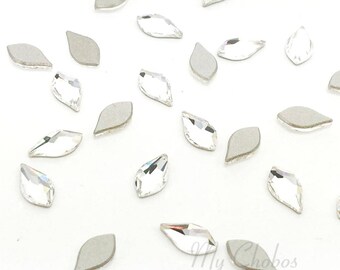 May include: A collection of clear crystal rhinestones in a teardrop shape. The rhinestones are scattered on a white surface.