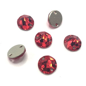 May include: Six red sew-on rhinestones with two holes each. The rhinestones are round and have a faceted design. There are also two silver sew-on settings with two holes each.
