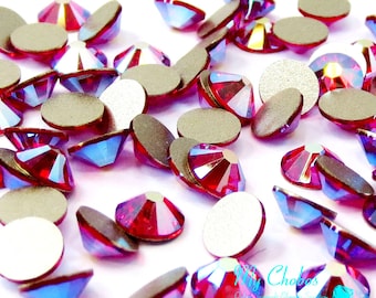 May include: A close-up of a pile of red iridescent glass rhinestones with silver backing. The rhinestones are scattered on a white surface.