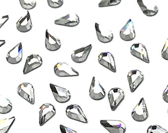 May include: A scattering of clear teardrop-shaped rhinestones on a white background.