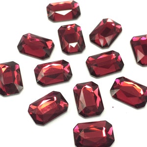 May include: Twelve red rectangular rhinestones with a faceted finish.