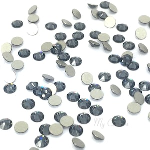 Puede incluir: Una dispersión de piedras de cristal negras con facetas iridiscentes, algunas con respaldo adhesivo, sobre una superficie blanca.