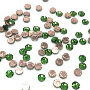 May include: Assortment of green and copper coloured rhinestones. The rhinestones are scattered on a white surface.