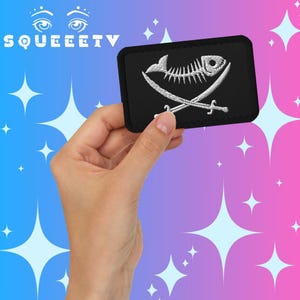 May include: A black rectangular patch featuring a white embroidered design of a fish skeleton and crossed swords. The patch is held in a hand against a blue and pink background with white star shapes. The word "SQUEEETV" is at the top.