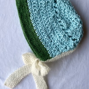 May include: A crocheted baby bonnet in light blue and green with a white crocheted bow.