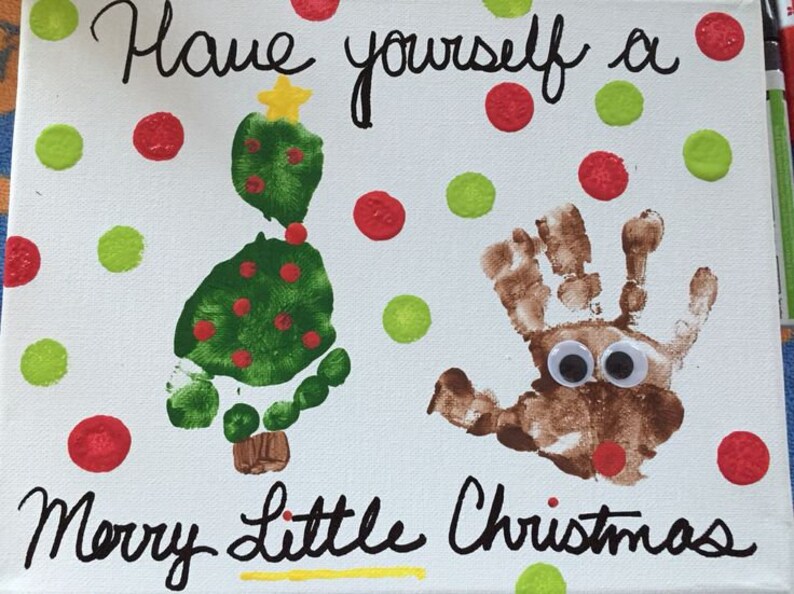 May include: A white canvas with the text "Have yourself a Merry Little Christmas" written in black marker. A green handprint tree with red dots and a yellow star on top is on the left side of the canvas. A brown handprint reindeer with googly eyes is on the right side of the canvas. The canvas is decorated with red and green dots.