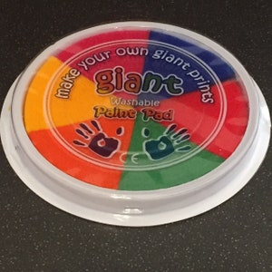 May include: A round, multi-colored washable paint pad with the words "Make your own giant prints" and "Giant Washable Paint Pad" printed on it. The pad has five sections of paint: yellow, orange, red, green, and blue.