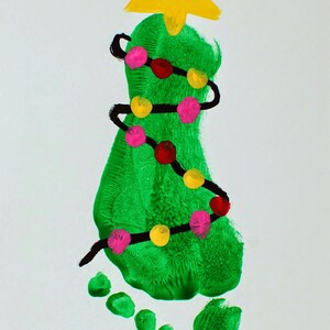 May include: A green handprint shaped like a Christmas tree with a yellow star on top. The tree is decorated with a black string of lights with pink and yellow bulbs.