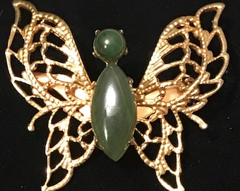 May include: A gold butterfly brooch with a green jade stone in the centre.
