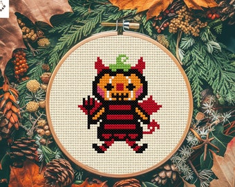 May include: A cross stitch pattern of a cute pumpkin dressed as a devil. The pattern is in a wooden embroidery hoop and is surrounded by fall leaves.