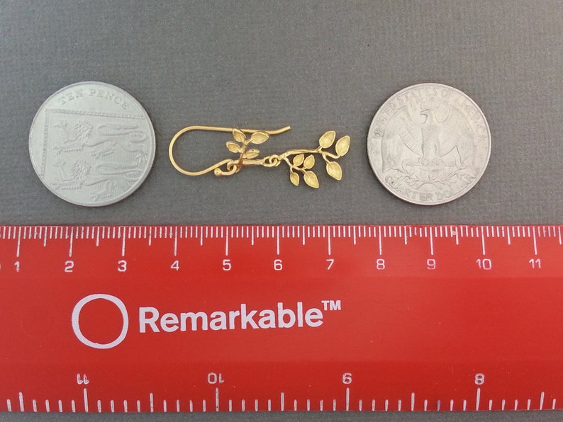 May include: Gold leaf earrings with a delicate branch design. The earrings are approximately 2.5 cm long and are shown next to a ruler and two coins for size reference.