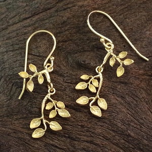 May include: Gold dangle earrings with a delicate branch design featuring multiple small leaves.