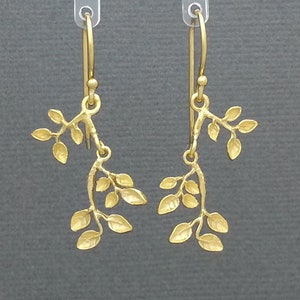 May include: A pair of gold-toned dangle earrings featuring a delicate branch design with multiple leaves. The earrings are made of metal and have a simple, elegant style.