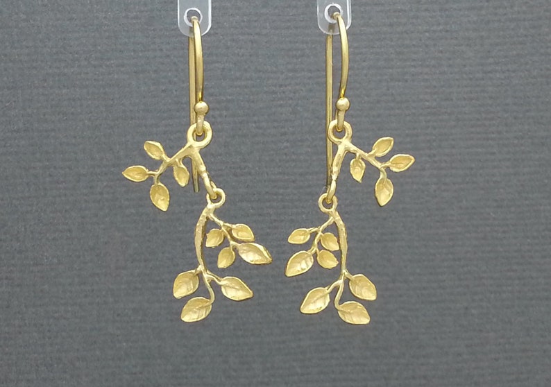 May include: A pair of gold-toned dangle earrings featuring a delicate branch design with multiple leaves. The earrings are made of metal and have a simple, elegant style.