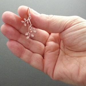 May include: Silver dangle earrings featuring a delicate branch design with multiple small leaves.