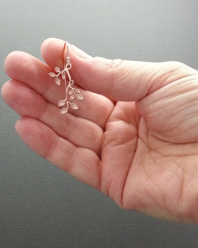 May include: Silver dangle earrings featuring a delicate branch design with multiple small leaves.