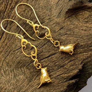 May include: Gold-coloured earrings with a bird charm and an openwork design. The earrings have a hook closure. The bird charms are detailed and add a whimsical touch. The earrings are displayed on a wooden surface.