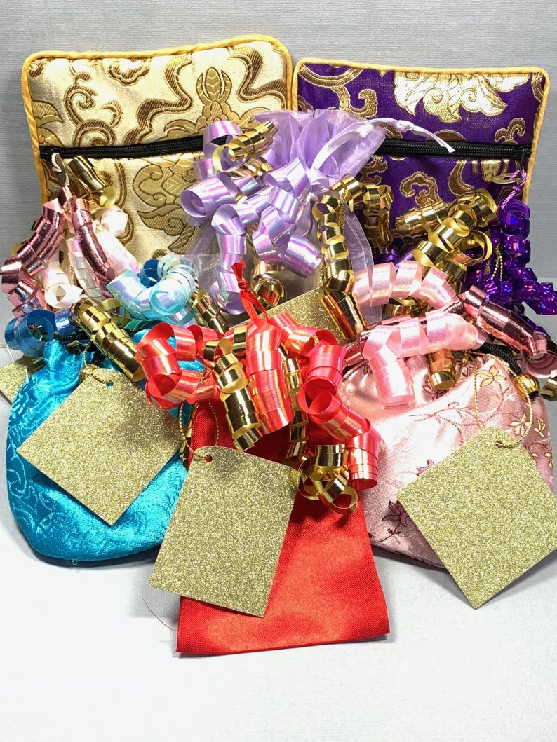 May include: Five small, colourful gift bags with gold, purple, pink, blue, and red fabric. Each bag has a gold tag attached and is decorated with ribbons and bows in various colours.