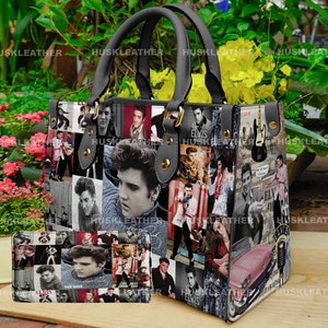 May include: A black leather handbag with a collage of Elvis Presley images. The bag has a top handle and a zipper closure. The images include Elvis in various poses, including singing, playing guitar, and wearing sunglasses. The bag also features the text "Elvis" and "ELVIS" in different fonts and sizes.