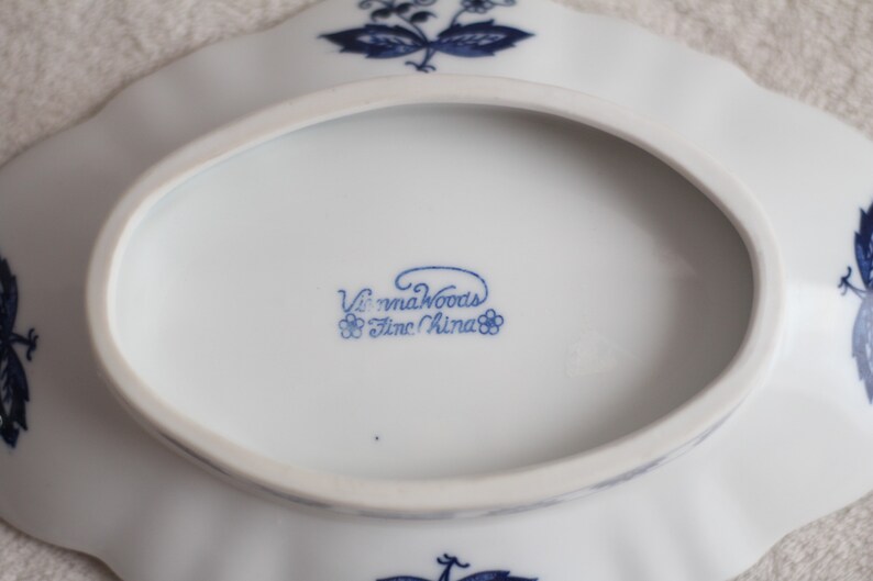 May include: A white oval serving dish with a blue floral design and the words "Vienna Woods Fine China" on the bottom.
