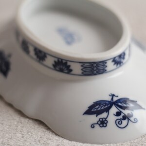 May include: A white ceramic bowl with a blue and white floral design. The bowl has a scalloped edge and a raised rim.
