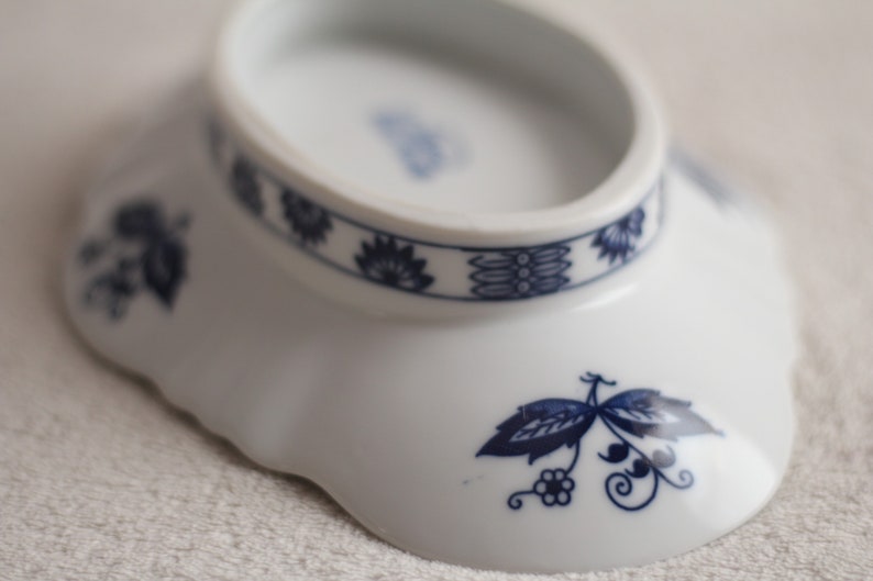 May include: A white ceramic bowl with a blue and white floral design. The bowl has a scalloped edge and a raised rim.