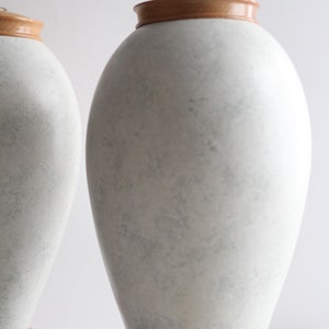 May include: Two white ceramic table lamps with wooden bases. The lamps have a textured, marbled finish and are in a contemporary style.