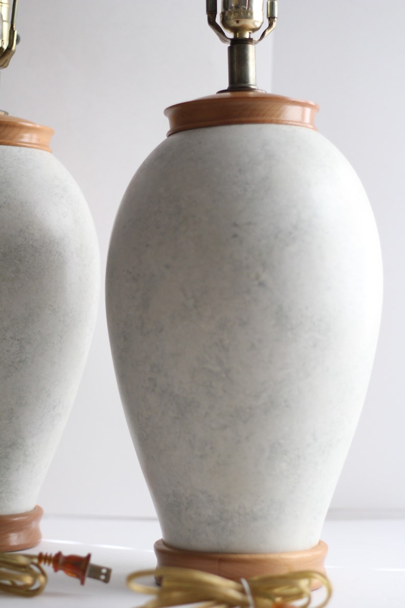 May include: Two white ceramic table lamps with wooden bases. The lamps have a textured, marbled finish and are in a contemporary style.