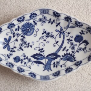 May include: A white oval ceramic dish with a blue and white floral pattern. The dish has a scalloped edge and features a dragonfly design.