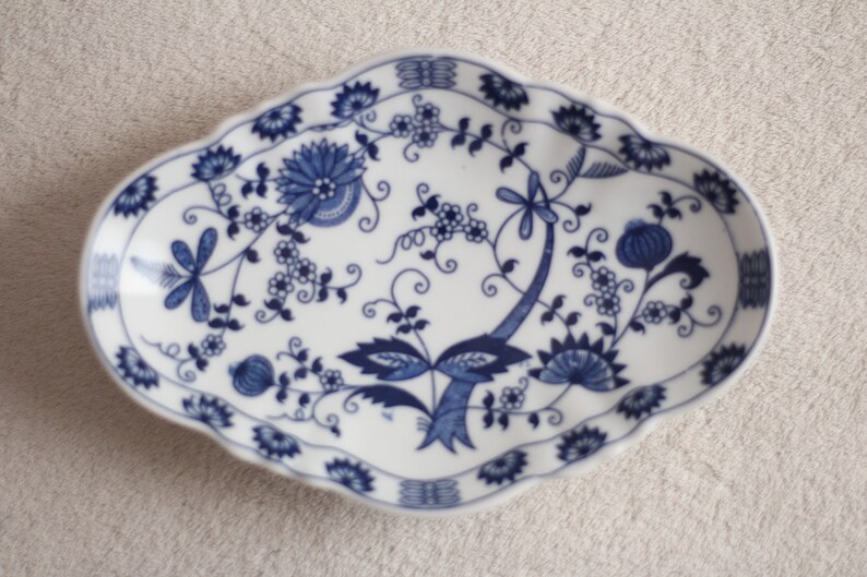 May include: A white oval ceramic dish with a blue and white floral pattern. The dish has a scalloped edge and features a dragonfly design.