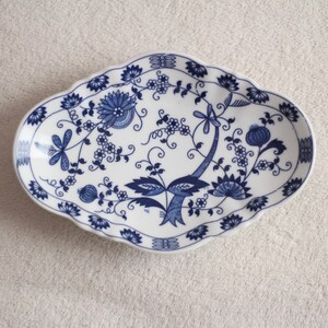 May include: A white oval ceramic dish with a blue and white floral design. The dish has a scalloped edge and is perfect for serving snacks or appetizers.
