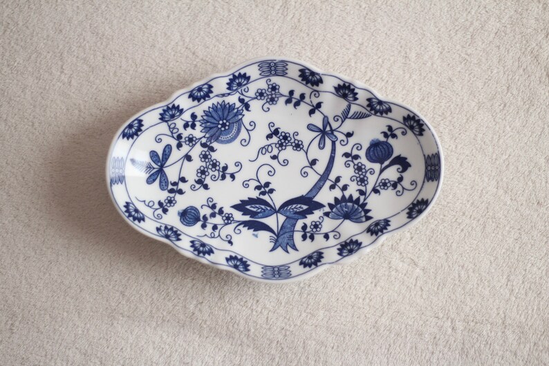 May include: A white oval ceramic dish with a blue and white floral design. The dish has a scalloped edge and is perfect for serving snacks or appetizers.