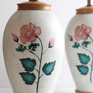 May include: Pair of ceramic table lamps with a white base and a wooden top. The lamps feature a hand-painted design of pink roses and green leaves.